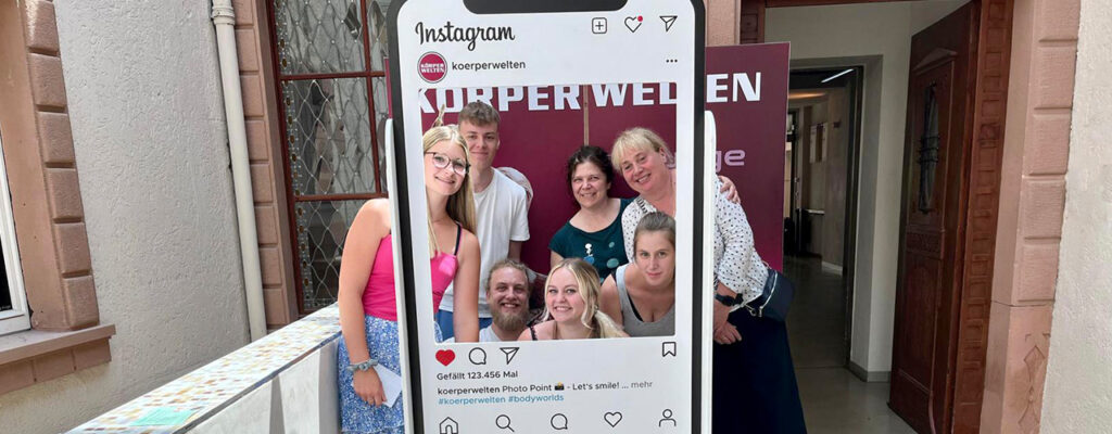 Schülerinnen und Schüler des Examenskurses in der Ausbildung Massage zu Besuch bei Körperwelten in Heidelberg. Gruppenfoto mit den Dozentinnen vor einem ausgeschnittenen Instagram Post