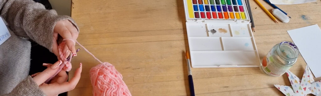 Nahaufnahme einer jungen Frau, die mit Wolle strickt und einem Farbkasten